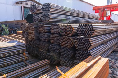 Galvanize demir borular ve paslanmaz çelik dikdörtgen metal çubuklar arka planda gantry vinç ile