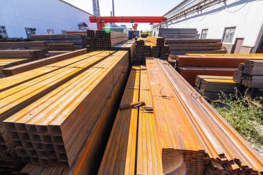 Galvanize demir borular ve paslanmaz çelik dikdörtgen metal çubuklar arka planda gantry vinç ile