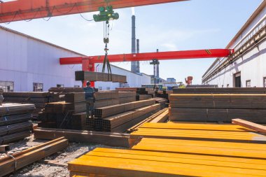 İşçi çelik fabrikasında kanatlı vinç taşıyan metal borular taşıyor.