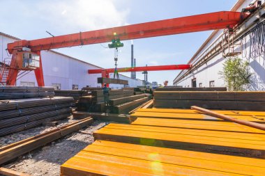 İşçi çelik fabrikasında kanatlı vinç taşıyan metal borular taşıyor.