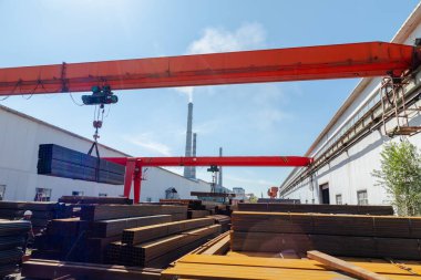 İşçi çelik fabrikasında kanatlı vinç taşıyan metal borular taşıyor.