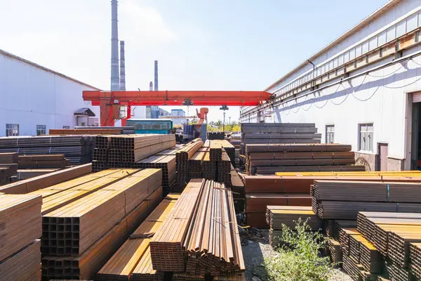 stock image Galvanized iron pipes stack and stainless steel rectangular bars of metal with gantry crane in the background