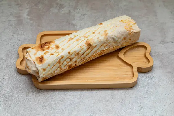 stock image A grilled shawarma wrap on a wooden tray, featuring a golden brown exterior and savory filling