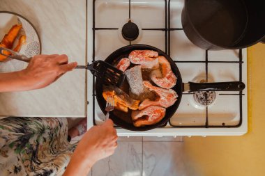 Elleri çatallı ve somon balığını tavada kızartıyordu. Evdeki gaz sobasında.