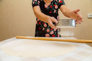 Masada hamurun üzerinde süzgeçle un karıştıran bir kadın.