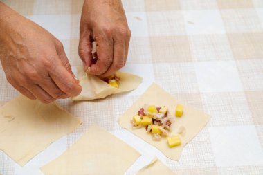 Kadın eli, manti pişirmek için dilimlenmiş hamur parçalarını kapatıyor.