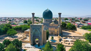 Samarkand, Uzbekistan - July 15, 2024: Aerial view of the historic Amir Temur Mausoleum Gur-i Amir Complex with its blue dome, surrounded by the cityscape and mountains clipart