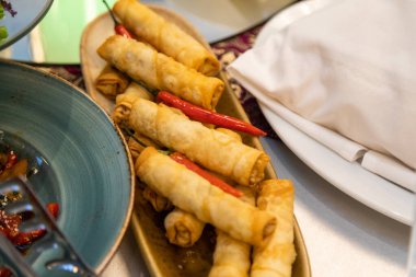 Sebzelerle dolu çıtır börekler, kırmızı biberlerle süslenmiş oval bir tabakta sunuluyor.