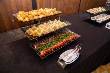 Muhtelif servis tabakları kruvasan, sandviç üçgenleri ve roka kaplı vişneli domatesleri sergiliyor. Zarif siyah tepsilerde güzelce düzenlenmiş.