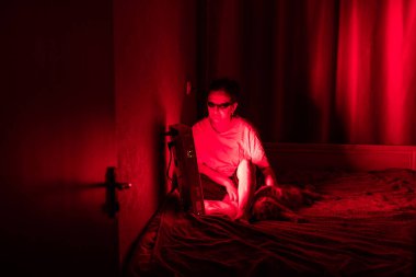 Yaşlı kadın kırmızı ışık terapi paneliyle bacağını tedavi ediyor ve evde kedi beslerken göz koruması takıyor.