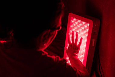 Closeup of Senior Woman touching Red Light Therapy Panel LEDs with hand clipart