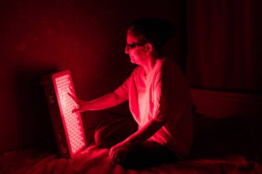 Senior Woman touching Red Light Therapy Panel LEDs with hand clipart