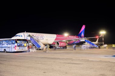 Bishkek, Kırgızistan - 14 Ekim 2023: Yolcular gece Manas Havaalanı 'ndan Wizz Air uçağına binerek, merdivenleri ve otobüsü kullanarak. Görülebilir farklı insan grupları