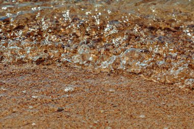 Kıyıdaki sığ sulara yaklaş. Yumuşak dalgalar kumsaldaki sıcak sarı kumun üzerinde kırılıyor.