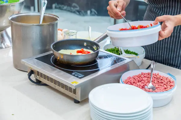 stock image Chef preparing omelets at a live cooking station, with ingredients like tomatoes and diced meat ready