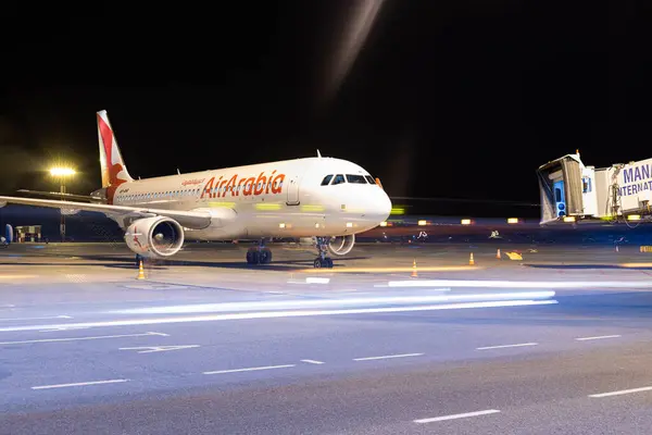 stock image Bishkek, Kyrgyzstan - October 14, 2023: An Air Arabia aircraft is parked at Manas International Airport at nighttime. The plane is connected to the terminal via an aerobridge, with motion blur lights