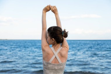 Spordaki rahat kadın temiz hava soluyor ve kumsalda kollarını açıp suya bakıyor, özgürlük kavramı.