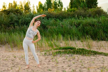 Dışarıda egzersiz yapan, antrenmandan önce ısınan formda bir kadın. Kollarını uzat ve uzaklara bak.