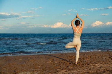 Genç ve güzel bir kadın dışarıda yoga yapıyor. Gölün kıyısında duruyor. Ağaç duruşu ile suya bakıyor. Uyum, kişisel bakım, rahatlama egzersizleri, sağlıklı yaşam tarzı ve meditasyon konsepti, zen akıl sağlığı