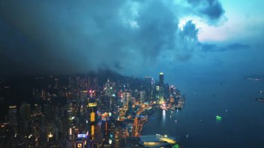13 Mayıs 2024 - Hong Kong, Çin: Gökyüzünde kara bulutlar oluşturan aydınlık gökdelenler ve canlı şehir ışıklarının yer aldığı alacağı alacakaranlıkta Hong Kong 'un ufuk çizgisinin ve limanın havadan görünüşü