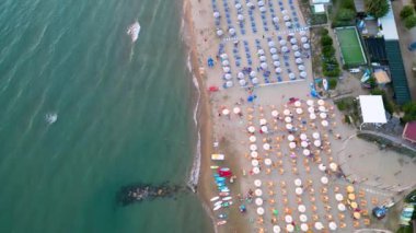Plaj şemsiyeleri ve şezlonglarıyla kumlu sahilin aşağı havadan görünüşü.