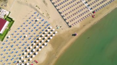 Plaj şemsiyeleri ve şezlonglarıyla kumlu sahilin aşağı havadan görünüşü.