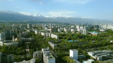 Güneşli bahar gününde, arka planda karla kaplı dağlarla Almaty şehrinin hava manzarası.