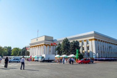 Bişkek, Kırgızistan 31 Ağustos 2024: İnsanlar bir sanayi fuarı sırasında önünde park halindeki satıcılar, kamyonlar ve arabaların olduğu bir binanın yakınında yürüyorlar