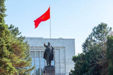 Bişkek, Kırgızistan - 31 Ağustos 2024: Kırgızistan 'da büyük bir bayrağın önünde yürüyen ve meydanda dinlenen insanların olduğu Lenin heykeli