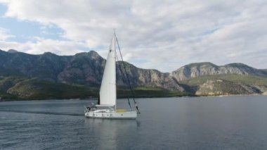 Okyanusta yüzen bir yatın havadan görünüşü. Pruvanın kenarında duran bir insan.