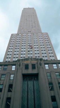 New York, ABD - 19 Aralık 2019: Düşük açılı Empire State Binası ön planda Amerikan bayrağı olan bulutlu bir gökyüzüne karşı