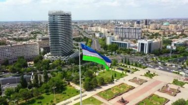 Taşkent, Özbekistan - 13 Haziran 2024: Çağdaş ve tarihi mimarinin yer aldığı Taşkent kentinin üzerinde belirgin bir şekilde dalgalanan Özbekistan bayrağının havadan görünüşü