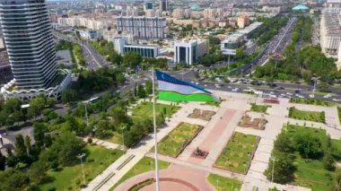 Taşkent, Özbekistan - 15 Temmuz 2024: Özbekistan bayrağıyla çevrili Uluslararası Dostluk Meydanı, modern binalar ve işlek yollarla çevrili