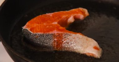 Bir parça somon balığı sıcak tavada kızartılıyor ve ev mutfağında cızırdayan yağ var.