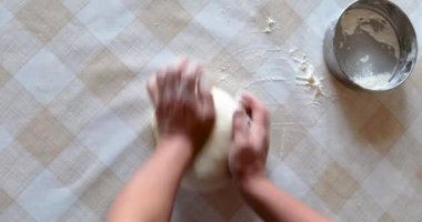 Masada hamurun üzerinde süzgeçle un karıştıran bir kadın.