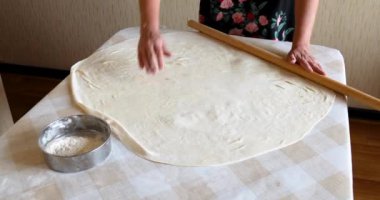 Masaya raptiye takmış hamuru yuvarlayan bir kadın.