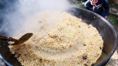 Tanınmayan adamın elleri pirinç palomuyla Kazan 'daki büyük spatulayı karıştırıyor.