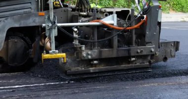 Yolda taze asfalt döşeyen bir asfalt kaldırım makinesinin detaylı görüntüsü. Makine, altyapı geliştirme projesinin bir parçası.