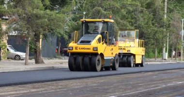 Bişkek, Kırgızistan - 14 Ağustos 2024: Yeni kaldırım döşeyen sarı pnömatik asfalt silindirli yol yapımı