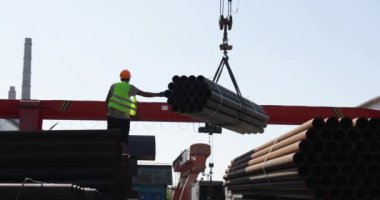 İşçi çelik fabrikasında kanatlı vinç taşıyan metal borular taşıyor.