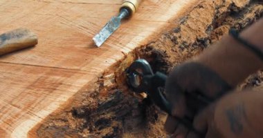 Marangoz, ağaç gövdesinden penseyle metal nesneyi kaldırıyor. El yapımı reçine ve ahşap masa.