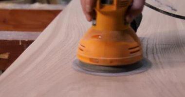 Bir atölyede marangozun ahşap masayı zımparalamasına yakın çekim.