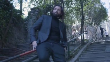 Takım elbiseli yakışıklı sakallı adam merdivenlerde ağır çekimde oturuyor.