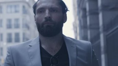 Sokakta ağır çekimde yürüyen takım elbiseli yakışıklı sakallı adamın yakın çekimi.