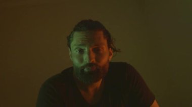 Kameraya bakıp, yeşil ve turuncu renkte yavaş çekimde yüzünü buruşturan çılgın sakallı adamın yakın çekimi.