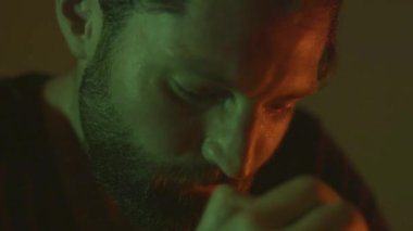 Hayal kırıklığına uğramış sakallı adamın yüzlerine dokunduğu karanlık odada yeşil ve turuncu renkler yavaş çekimde.