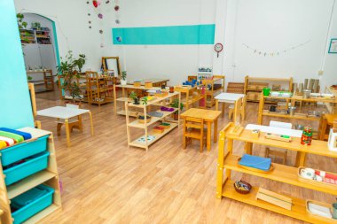 Renkli bir Montessori anaokulu sınıfı, ahşap mobilyalar ve eğitim malzemeleriyle dolu. Bitkiler ve dekorasyonlar misafirperver bir ortam yaratır..