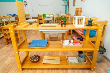 Bardaklar, çanaklar ve çocuk gelişimi için araç gereçler gibi organize eğitim materyalleriyle rafların yer aldığı ahşap Montessori sınıfı kurulumu