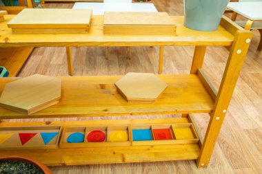 Tahta Montessori rafında geometrik şekiller, altıgen bulmacalar ve duyusal aktiviteler için renkli parçalar var.