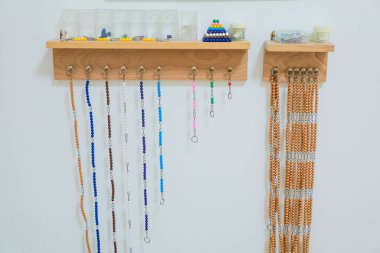 Tahta Montessori matematik boncukları ve boncuk zincirler duvarlara monte edilmiş bir rafta sergileniyor. Matematik kavramları ve saymayı öğrenmek için gerekli.